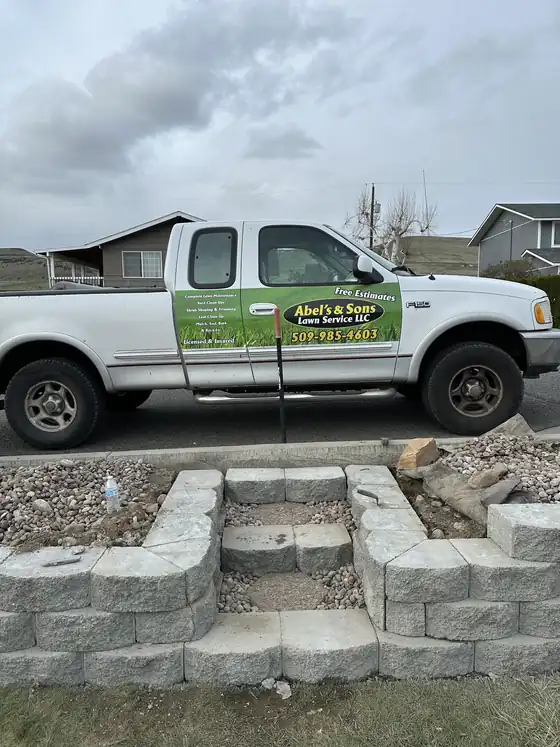 Abel's & Sons pickup with the oval logo, Free Estimates and 509-985-4603 on the door, parked above new block steps