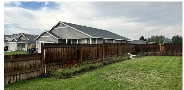 Weathered brown wood privacy fence along a backyard lawn before replacement